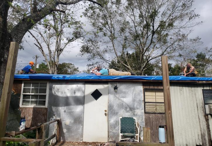 Three team members work to apply a tarp to the roof of a home.